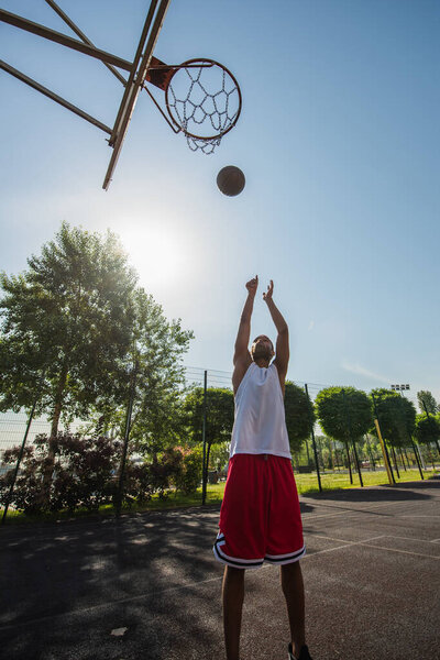 Wide angle view of african american player throwing ball in basketball hoop outdoors 