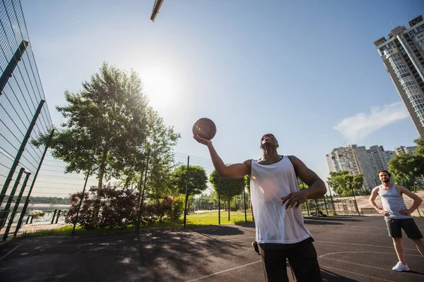 笑顔アフリカ系アメリカ人男保持バスケットボールボール近く友人オン遊び場 — ストック写真