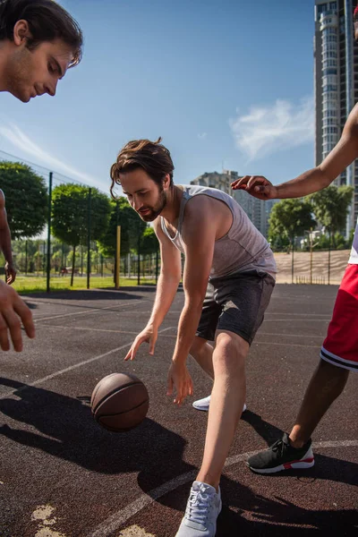 Çok ırklı sporcular dışarıda, oyun alanında birlikte basketbol oynuyorlar. 