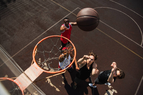 Overhead view of interracial men with raised hands playing basketball under hoop 