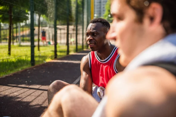 Lächelnder Afrikanisch Amerikanischer Sportler Sitzt Neben Verschwommenem Freund Vordergrund — Stockfoto
