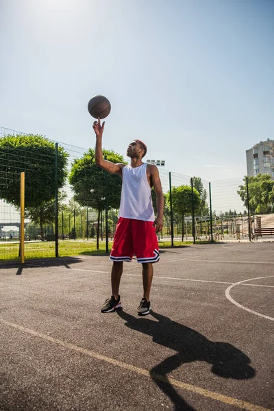 サイドビューのアフリカ系アメリカ人スポーツマン保持バスケットボールボール上の指で遊び場 — ストック写真