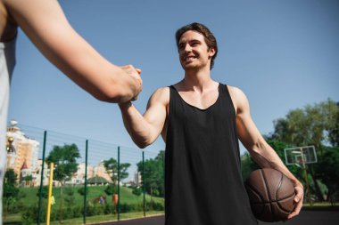 Arkadaşını basketbol topuyla selamlayan gülümseyen sporcunun düşük açılı görüntüsü. 