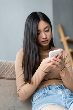 Asyalı kadın yatak odasında cep telefonuyla mesajlaşıyor.
