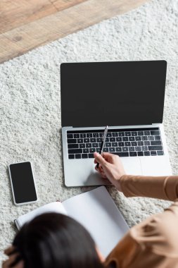 Bulanık bir kadının akıllı telefonun yanındaki dizüstü bilgisayara kalemle işaret ettiği yerde boş ekran var.