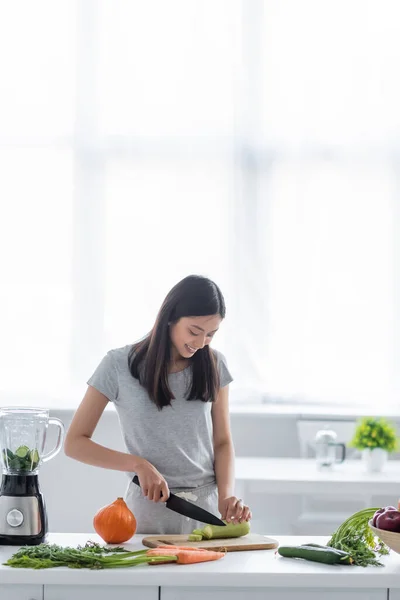 亚洲女人很高兴在厨房的生菜和电动搅拌器旁边切新鲜的拉链 — 图库照片