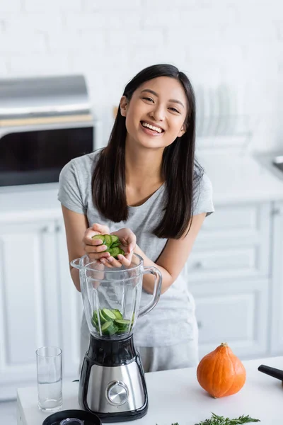 Joyful Asian Woman Adding Sliced Cucumber Blender While Preparing Breakfast — Stock Photo, Image
