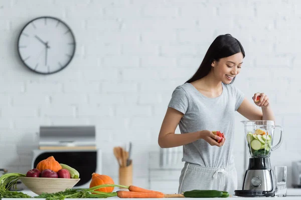 幸せアジアの女性は台所で新鮮な野菜の近くにスライスズッキーニとシェーカーにリンゴを追加します — ストック写真