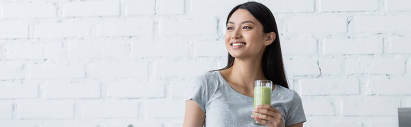 young asian woman with glass of fresh smoothie smiling while looking away, banner