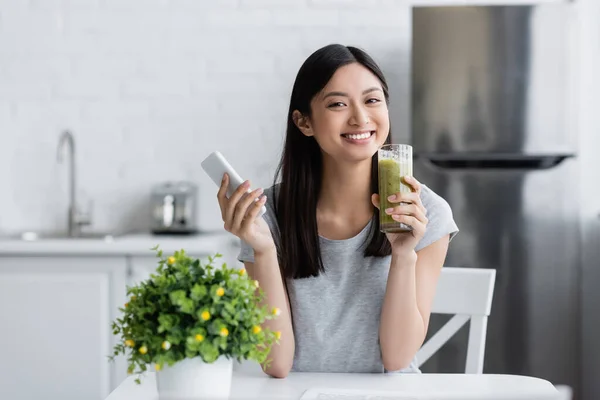 Happy Asian Woman Holding Cellphone Glass Homemade Smoothie Blurred Potted — Stock Photo, Image