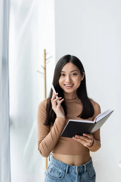 Sorrindo Mulher Asiática Com Notebook Falando Smartphone Enquanto Olha Para — Fotografia de Stock