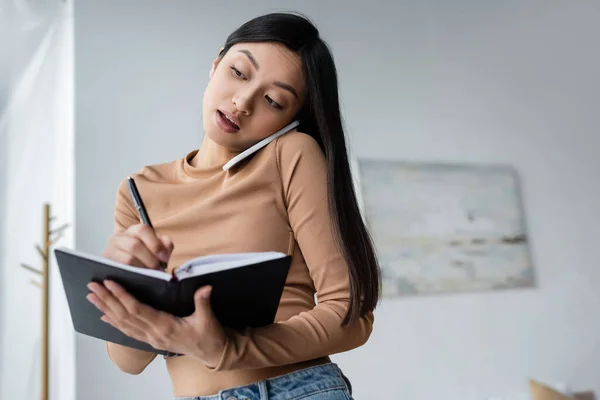 Mujer Asiática Escribiendo Cuaderno Durante Conversación Teléfono Móvil Casa —  Fotos de Stock