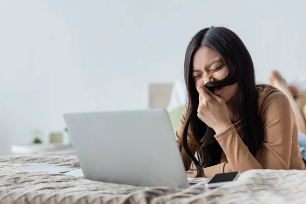 Cheerful Asian Woman Covering Face Hair Blurred Laptop Bed — Stock Photo, Image