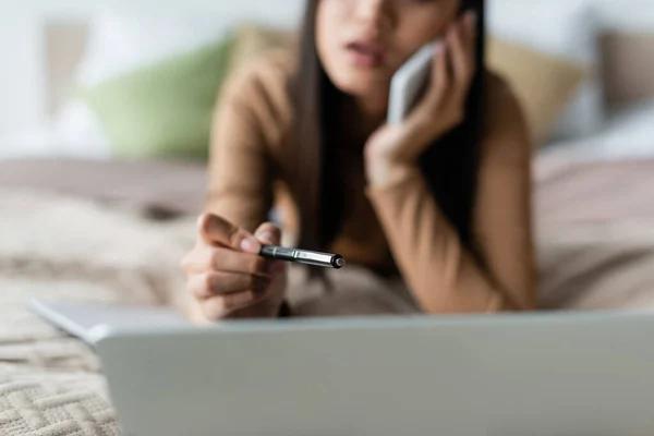 Blurred Woman Pointing Pen Laptop While Talking Cellphone Bedroom — Stock Photo, Image