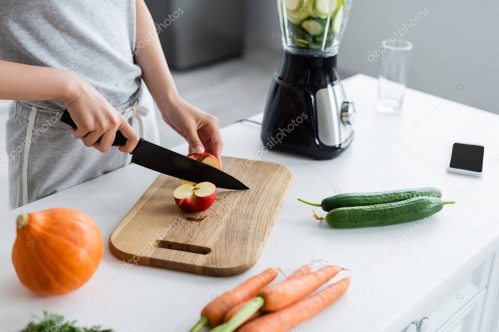 partial view of woman cutting apple near pumpkin, cucumbers and carrots on kitchen table