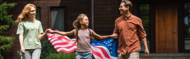 Amerikan bayrağı taşıyan çocuklar ve ebeveynler açık havada el ele tutuşuyorlar. 