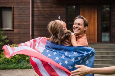 Mutlu baba çocuğu kucağında, açık havada Amerikan bayrağı taşıyor. 