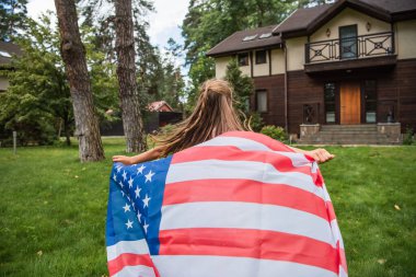 Arka planda, çimenlerde koşarken Amerikan bayrağı tutan bir kız var. 