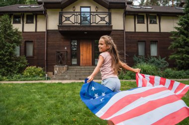 Evin yanında koşan Amerikan bayrağı taşıyan çocuğun yan görüntüsü 