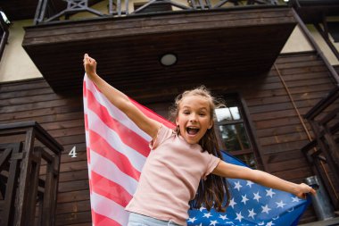 Amerikan bayrağı taşıyan heyecanlı çocuk tatil evinin yakınındaki kameraya bakıyor. 