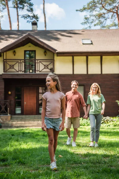 Glückliches Kind Spaziert Auf Rasen Neben Verschwommener Familie — Stockfoto