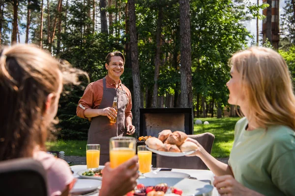 笑顔男とともにビール立って近くにぼやけた妻と子供とともにオレンジジュース屋外 — ストック写真