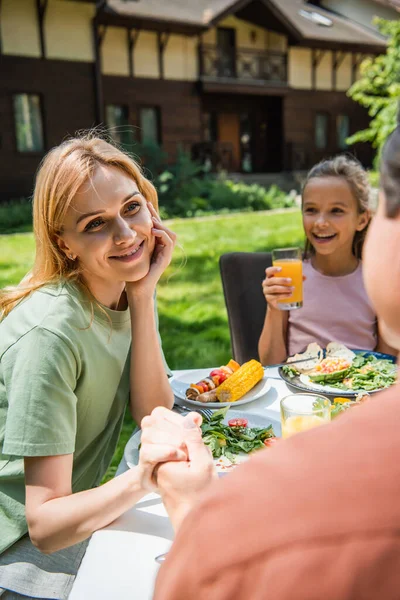 笑顔の女性保持手の手のぼやけた夫近く陽気な子供とともにオレンジジュースと食べ物屋外 — ストック写真