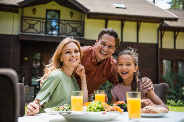 Cheerful family looking at camera near delicious food outdoors 