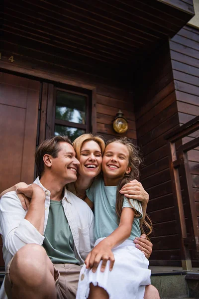 Smilende Familie Med Lukkede Øyne Som Omfavner Feriehusets Veranda – stockfoto