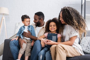 Neşeli Afrikalı Amerikalı çift evdeki kanepede otururken konuşuyor.