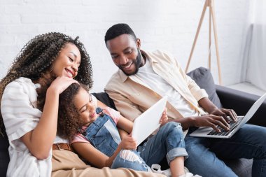 Mutlu anne ve babasının dizüstü bilgisayarını kullanan Afrikalı Amerikalı bir çocuk.
