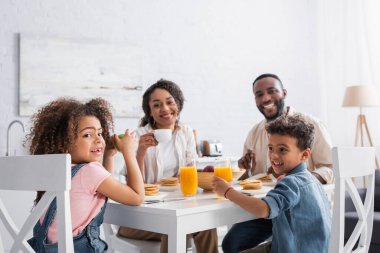 Mutlu Afro-Amerikan ailesi kahvaltıda kameraya gülümsüyor.