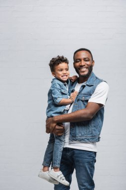  Neşeli Afrikalı Amerikalı adam kameraya gülümserken oğlunu griye sarıyordu.