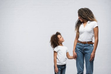 Kızı olan mutlu Afro-Amerikan bir kadın, griye el ele tutuşurken birbirine bakıyor.