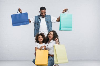 Heyecanlı Afro-Amerikan ailesi gri üzerinde renkli alışveriş torbaları taşıyor.