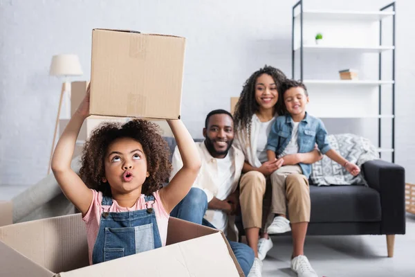 Excited African American Child Holding Cardboard Box Blurred Family — Stock Photo, Image