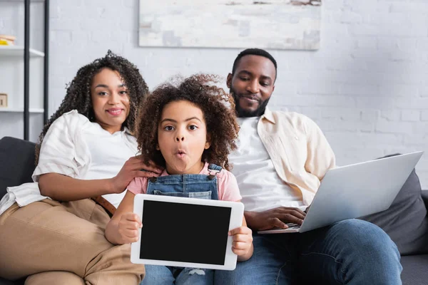 令人惊讶的非洲裔美国女孩在笑着的父母面前展示空白屏幕的数码平板电脑 — 图库照片