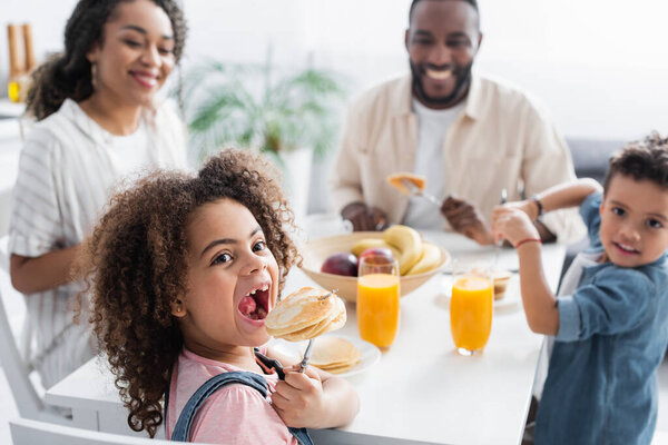 african american girl eating pancake near blurred family