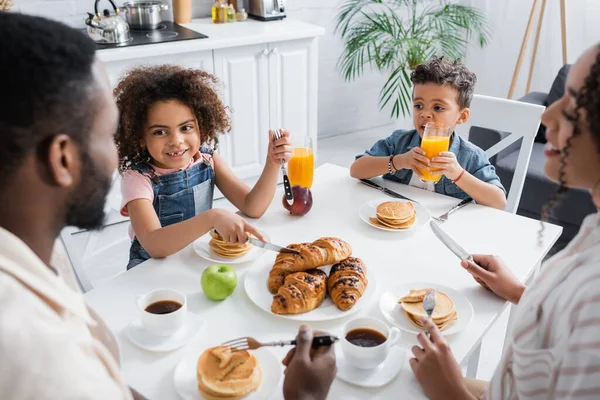 アフリカ系アメリカ人の女の子が朝食中に家族やクロワッサンに笑顔で — ストック写真