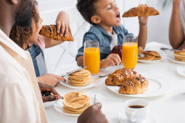 african american kids eating croissants for breakfast near blurred parents