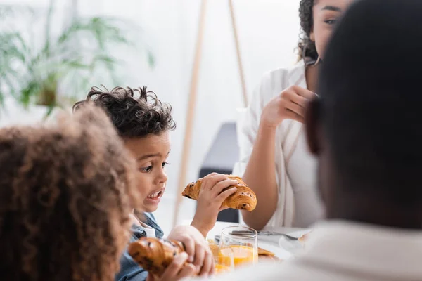 Opgewonden Afrikaanse Amerikaanse Jongen Houden Croissant Buurt Wazig Familie — Stockfoto