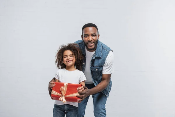 喜形于色的非洲裔美国小孩在喜形于色的爸爸身边展示红色礼品盒 — 图库照片