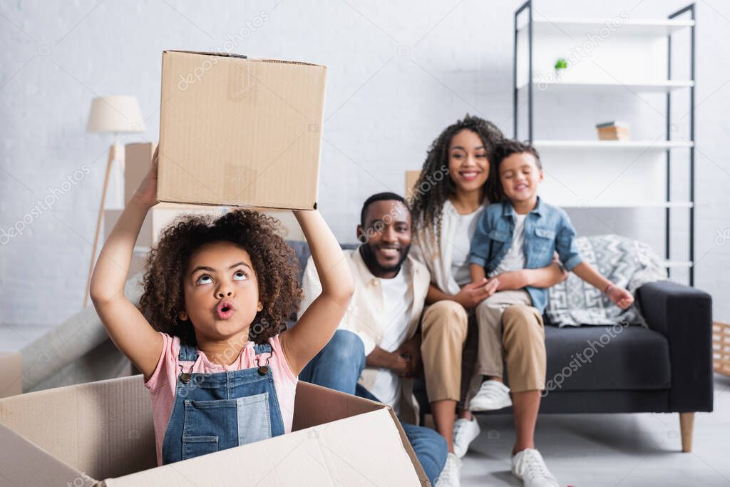 excited african american child holding cardboard box near blurred family