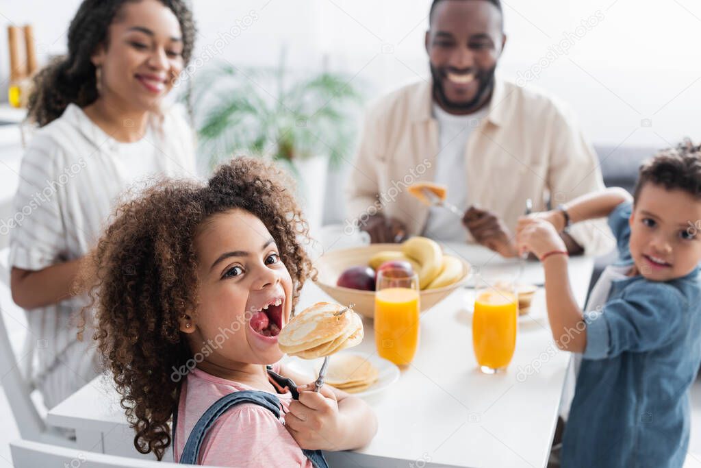 african american girl eating pancake near blurred family