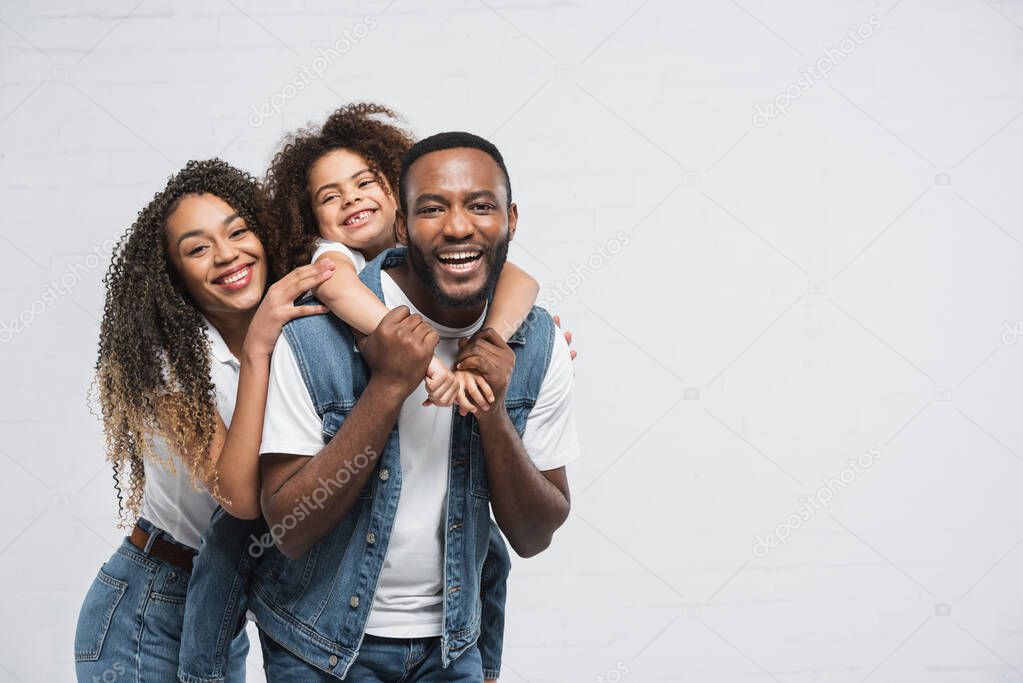 happy african american family looking at camera while hugging on grey