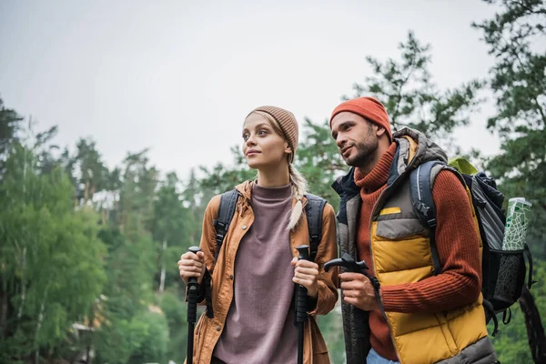 Couple Backpacks Holding Hiking Sticks Looking Away Forest — Stockfoto