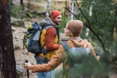 usmívající se muž s batohem při pohledu na ženu trekking v lese na rozmazané popředí 
