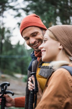 happy man looking at blurred and smiling girlfriend in forest 