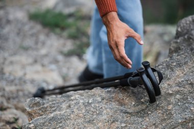 cropped view of man reaching hiking sticks on rock 