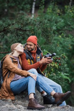 cheerful woman leaning on man holding vintage camera in forest 